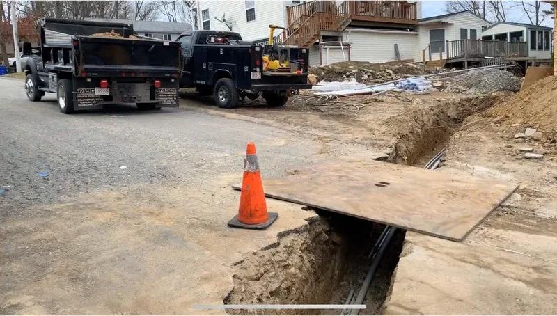 Utility trench with a steel plate and traffic cone beside dump trucks
