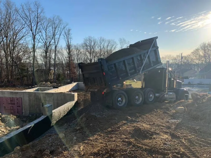Dump truck unloading fill beside a new foundation