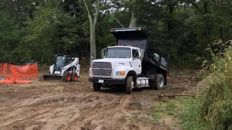 White dump truck and skid steer at a cleared site