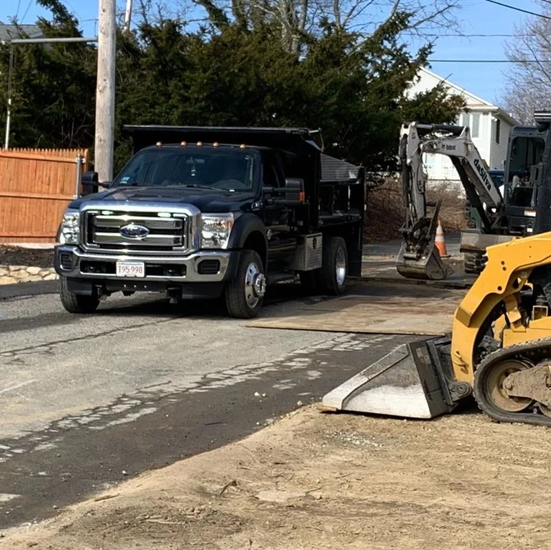 Black dump truck and skid steer on a residential street