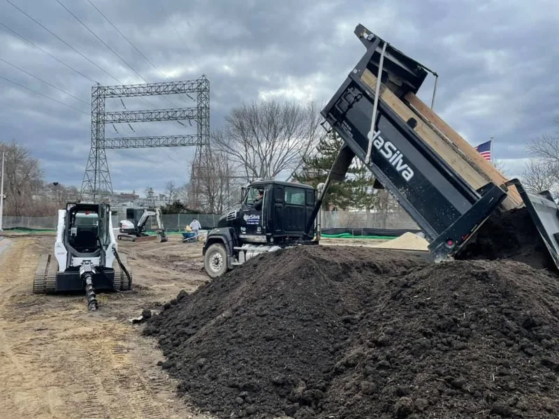 Dump truck unloading topsoil beside a skid steer