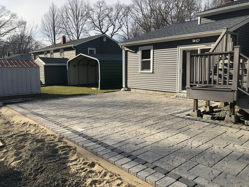 Paver patio being installed behind a gray home