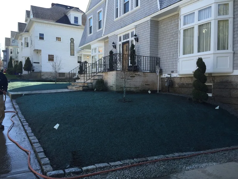 Newly hydroseeded front lawn edged with stone beside a white house