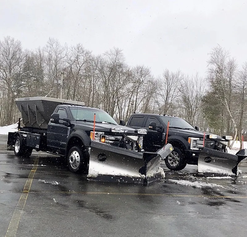 Two black pickup trucks with snow plows and salt spreader
