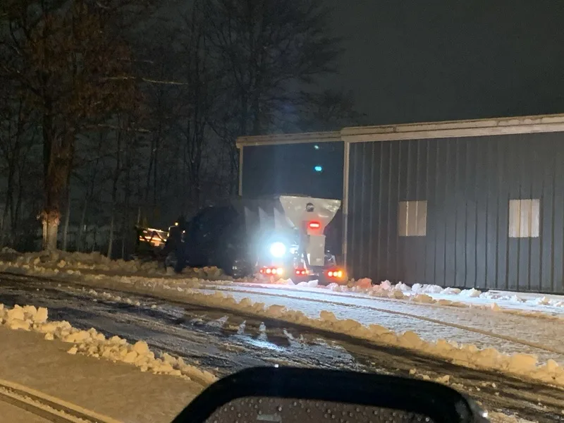 Salt spreader truck lit up at night beside a building